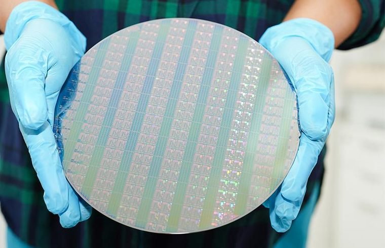 Gloved hand holding a semiconductor wafer inside a controlled production environment